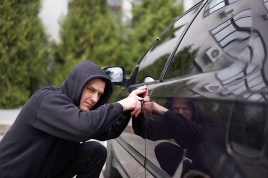 Car jacking thief steal car breaking door criminal job burglar Hijacks Auto thief black balaclava hoodie trying break into vehicle screwdriver Street crime violence gangster robber automobile parking