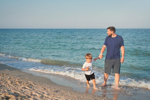 Dad holds son hand. Father Child spending time together sea vacation Young man little boy walking beach Fathers day. Family with one child. Happy childhood with daddy. Full lenght