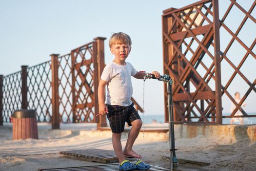 Child wash legs after beach sand Caucasian boy standing beach. Childhood summertime. Family vacation with one child.