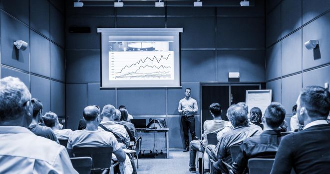 Speaker giving a talk in conference hall at business event. Unrecognizable people in audience at conference hall. Business and Entrepreneurship concept. Blue toned black and white.