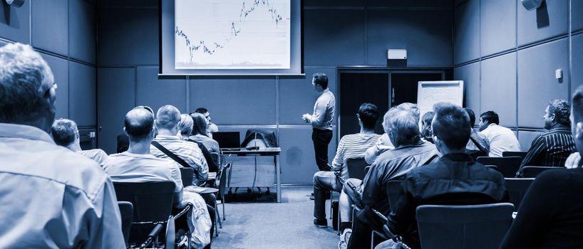 Speaker giving a talk in conference hall at business event. Unrecognizable people in audience at conference hall. Business and Entrepreneurship concept. Blue toned black and white.