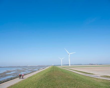 men on bicycle and wind turbines in rural landscape of schouwen duiveland in dutch province of zeeland under blue sky