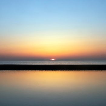 reflection of colorful sunset in water near beach on the dutch coast in holland