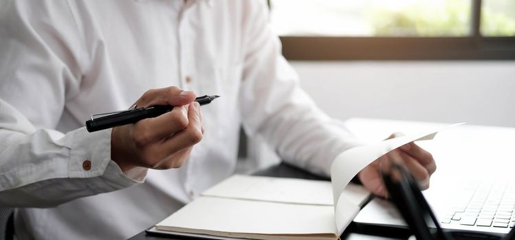 Closeup businessman writing on notebook on table with laptop..