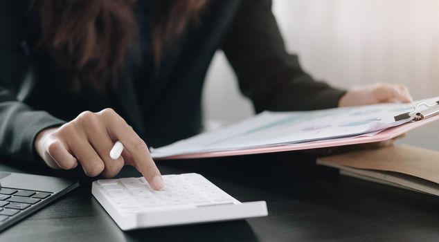 Close up Business woman using calculator and laptop for do math finance on wooden desk in office and business working background, tax, accounting, statistics and analytic research concept.