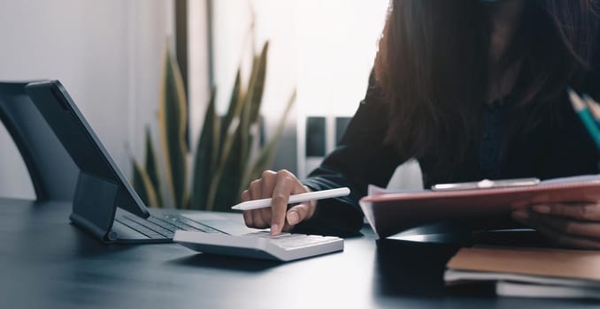 Close up Business woman using calculator and laptop for do math finance on wooden desk in office and business working background, tax, accounting, statistics and analytic research concept.