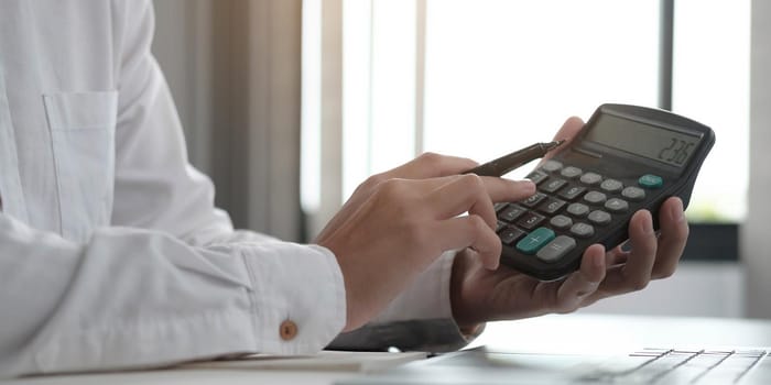 Close up Business woman using calculator and laptop for do math finance on wooden desk in office and business working background, tax, accounting, statistics and analytic research concept.