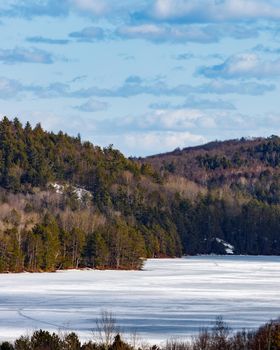 A high-angle view of Carson Lake, Ontario and surrounding hills. In this vertically-oriented landscape, the surface of the water is still frozen in late winter.