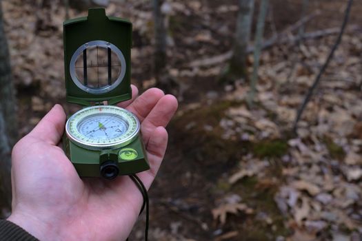 A hand is holding a prismatic compass and raising it for navigational use on a hiking trail in this point-of-view image.