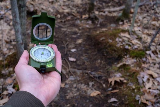 A point-of-view image showing an outstretched hand laying a prismatic compass flat upon it to navigate in the woods.