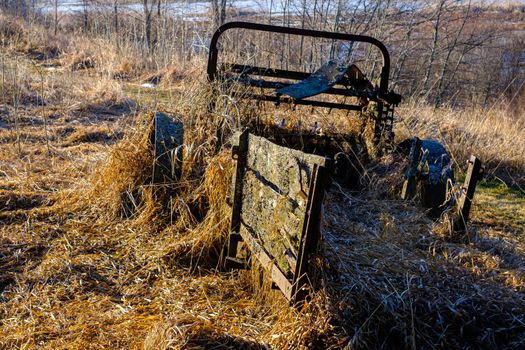 A derelict old manure spreader sits broken down and covered in dried grass, lichen and moss. The vintage, horse-drawn farm equipment features old rusted metal and wooden components.