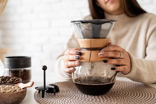 Alternative coffee brewing. Young woman brewing coffee in coffee pot standing at the white table with various stuff for alternative coffee brewing, pouring hot water into the filter
