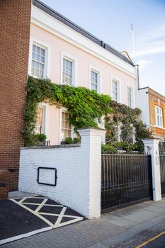 Front side of pink British house with white door and covered with climbing plants. Beautiful pastel pink English house with victorian architecture. Colorful London neighborhood
