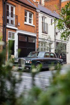 London, UK - February 14, 2020: Classic luxury car parked next to a ceramic dog and outside red brick British house. Dark green Rolls-Royce Silver Shadow parked on street. Classic European cars