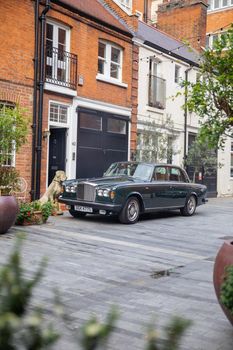 London, UK - February 14, 2020: Classic luxury car parked next to a ceramic dog and outside red brick British house. Dark green Rolls-Royce Silver Shadow parked on street. Classic European cars