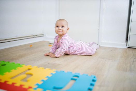 Adorable baby smiling and lying face down on wooden floor next to colorful children mat. Portrait of cute baby playing on the floor. Happy babies having fun
