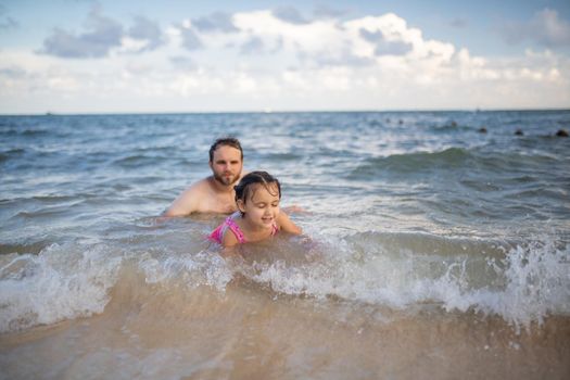 Happy father and young daughter joyfully playing in the water at the beach. Man and cute young child having fun in sea. Tropical summer vacations