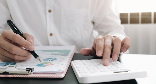 Close up Businessman using calculator and laptop for do math finance on wooden desk in office and business working background, tax, accounting, statistics and analytic research concept.