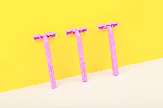 Pink razors on white table against yellow wall. Concept of shaving tools for safe shaving and smooth skin and body care