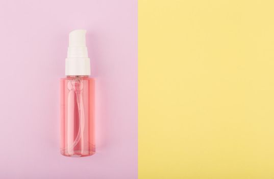 Foam or gel for skin cleaning and exfoliating in transparent tube with dispenser on pink and yellow background with copy space. Concept of skin care products for every day use