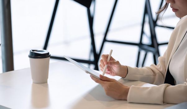 Close up businesswoman holds pen stylus drawing on digital tablet on workplace