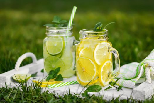 Cold refreshing homemade lemonade with mint, lemon and lime in mason jars on a summer lawn.