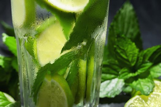 Fresh homemade mojito cocktail with lime, mint and ice on a black background, close-up.