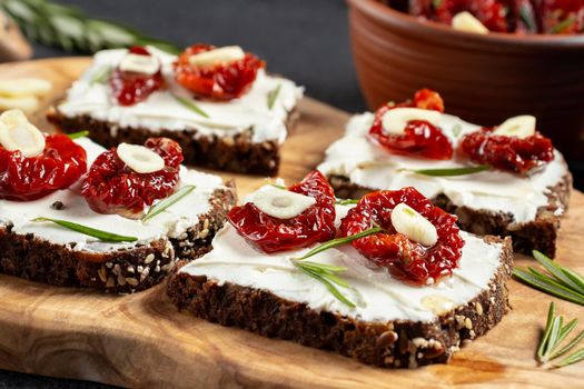 Homemade multigrain bread sandwiches with cream cheese and sun-dried tomatoes on a wooden platter, close-up. Healthy eating concept.