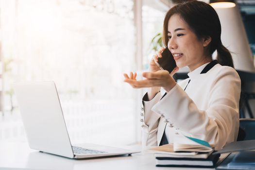 Asian business woman beautiful charming smiling using laptop and talking on phone at her office