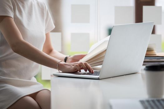 Cropped photo hand of woman writing making list taking notes in notepad working or learning online with laptop at home.