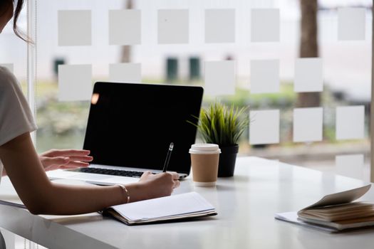 Close up of hand businesswoman writing on paper and using laptop to searching data for working or online learning.