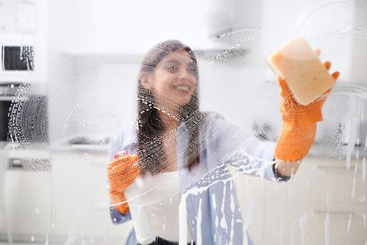 Smiling woman cleaning dirty window with special detergent. Concept of prevention coronavirus.