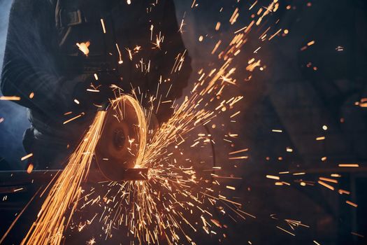 Close up of worker cutting metal pipe with large yellow sparks. Concept of working with angle grinder and polishing or welding metal in factory.