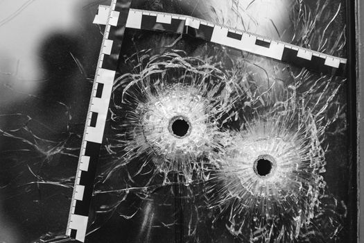 bullet holes in a glass shop window marked with a police tape.
