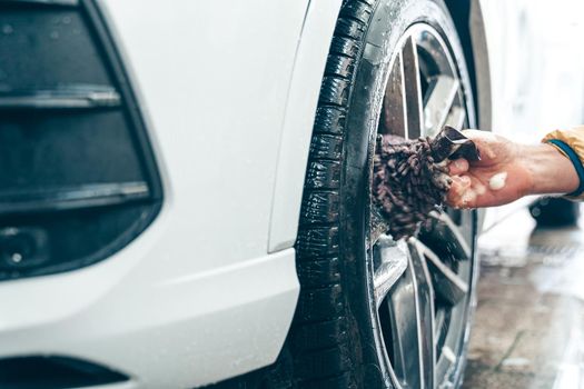 Manual car wheel cleaning with the help of sponges and foam.