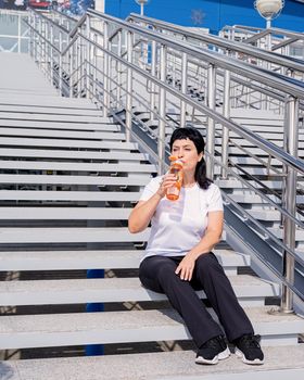 Sport and fitness. Senior sport. Active seniors. Smiling senior woman drinking water after workout outdoors on urban background