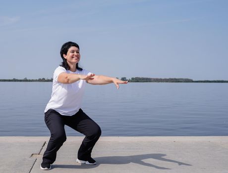 Sport and fitness. Senior sport. Active seniors. Active and happy senior woman squatting near the riverside