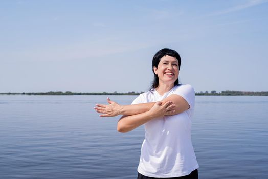 Sport and fitness. Senior sport. Active seniors. Active and happy senior woman doing stretching near the riverside