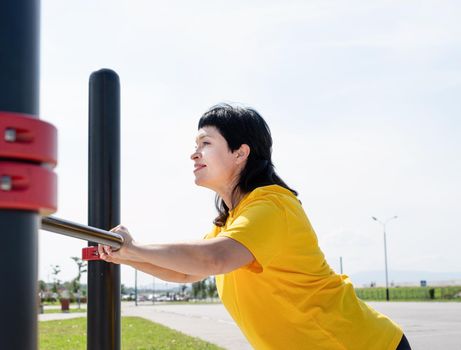 Sport and fitness. Senior sport. Active seniors. Smiling senior woman doing push ups outdoors on the sports ground bars