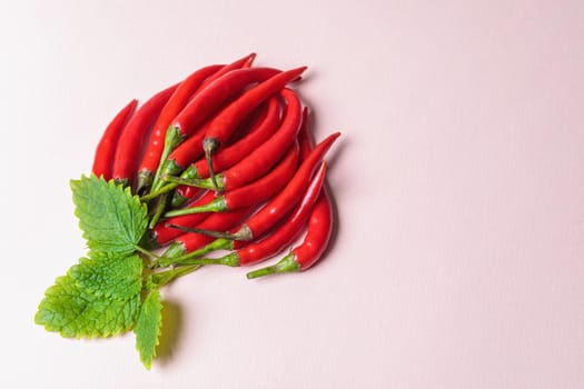 Slide of red chili peppers with green leaves on a light background. View from above.