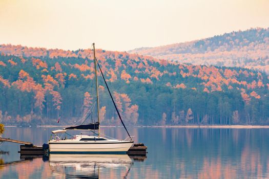 Sailing boat on a calm lake in the early morning against the backdrop of mountains. The mountains are covered with autumnal golden foliage