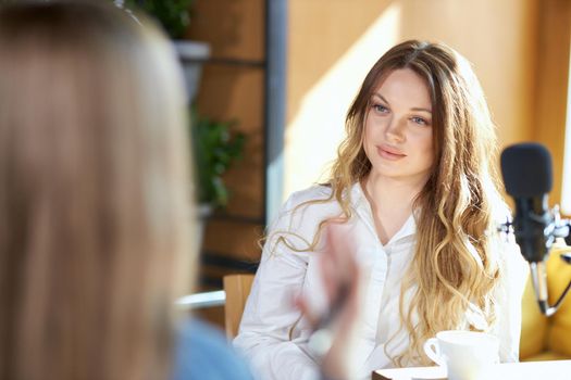 Side view of blogger woman giving interview with modern black microphone with cup coffee. Concept of process communicating about different topics in cafe. 