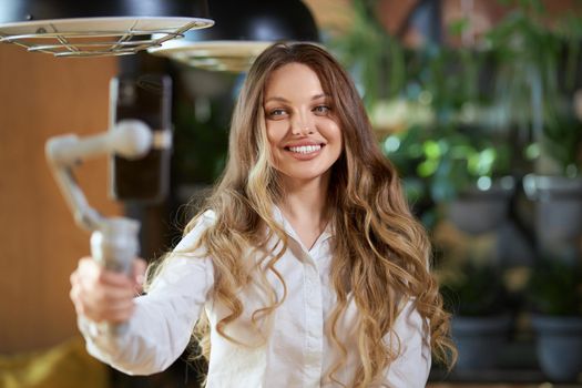 Close up portrait of cute and beautiful smiling woman in white shirt holding selfie stick and communicating with people on phone. Concept of good time with talking followers or friends online. 