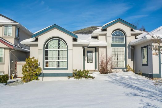 Luxury residential house with front yard in snow on winter sunny day