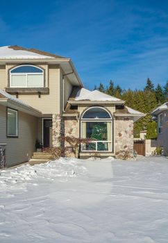 Entrance of luxury house with front yard in snow. Residential house on winter sunny day prepared for Christmas celebration