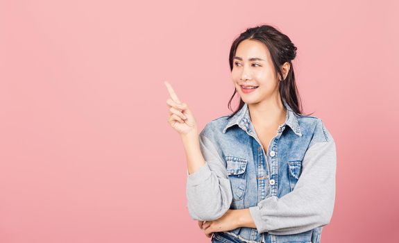 Happy Asian portrait beautiful cute young woman standing smiling indicate finger empty space looking to space, studio shot isolated on pink background, Thai female pointing index out with copy space