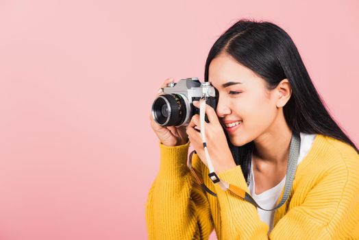 
Attractive energetic happy Asian portrait beautiful young woman smiling photographer taking a picture and looking viewfinder on retro vintage photo camera ready to shoot isolated on pink background