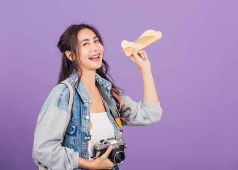 Happy Asian portrait beautiful young woman excited smiling holding airplane toy and retro vintage photo camera, Thai female ready travel trip isolated on purple background, tourism and vacation