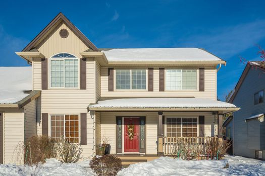 Entrance of luxury house with front yard in snow. Residential house on winter sunny day decorated for Christmas celebration
