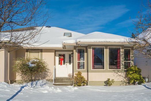 Entrance of luxury house with front yard in snow. Residential house on winter sunny day decorated for Christmas celebration